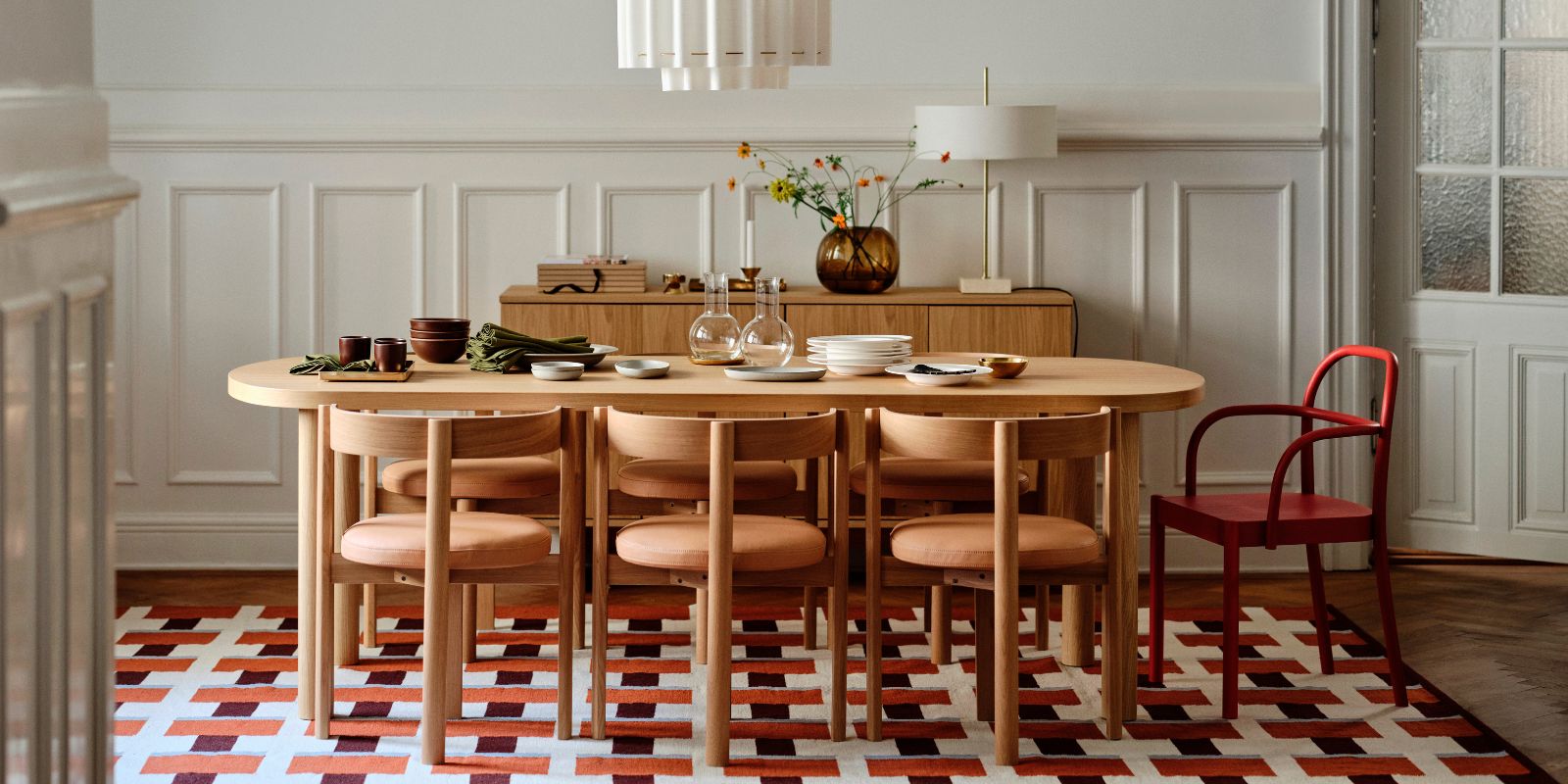 Comedor nórdico con madera cálida y piezas STOCKHOLM 2025: mesa, sillas, vajilla, cubiertos, florero y lámparas.