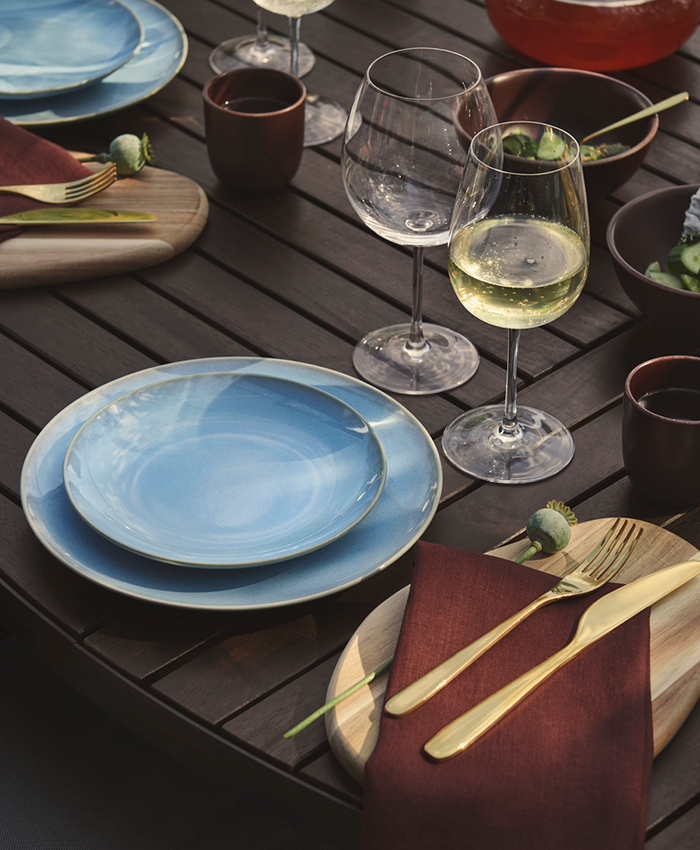 Elegant table setting featuring blue plates, wine glasses, and gold cutlery on a rustic dark wooden surface.