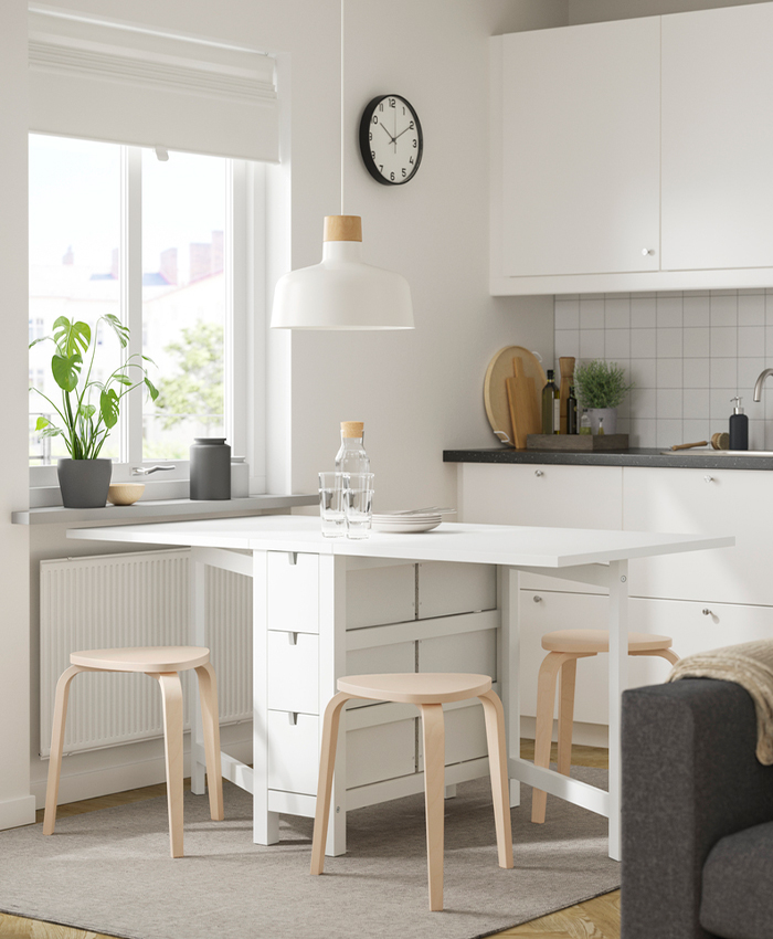 Cocina luminosa con mesa plegable blanca y taburetes de madera.