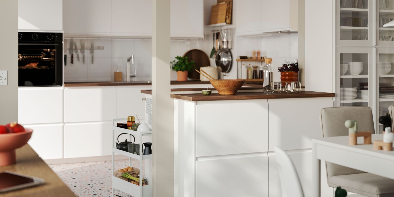 La luminosa cocina cuenta con frentes VOXTORP en blanco mate y una isla con una mesa de comedor blanca en primer plano.