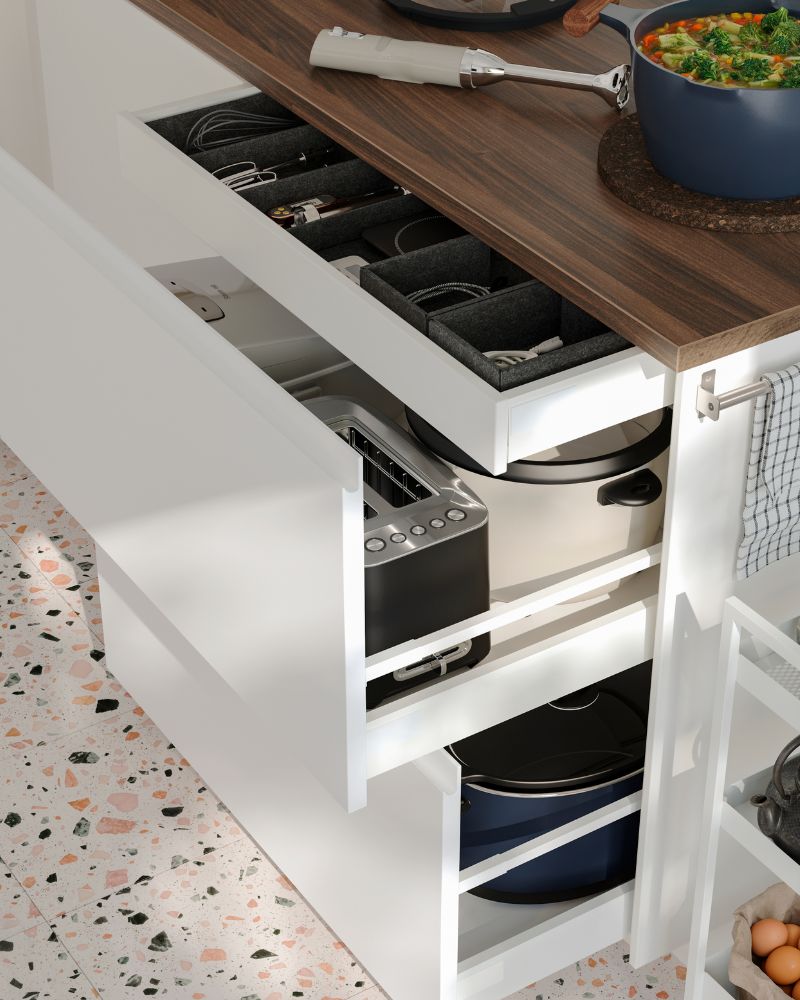 Se han abierto varios cajones de una península de cocina con frentes blancos VOXTORP, dejando a la vista los pequeños electrodomésticos que hay en su interior.