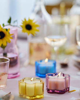 Colorful flower-shaped glass candle holders with lit candles decorate a festive and spring table.
