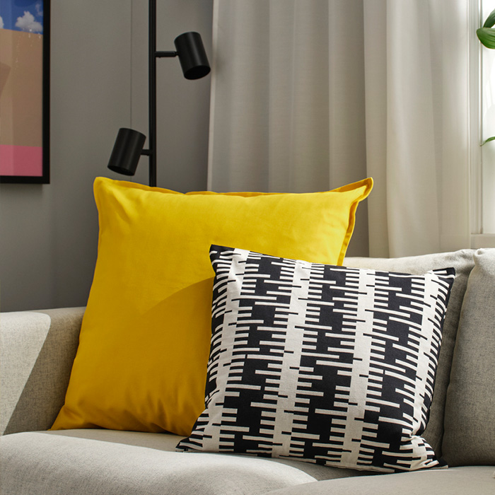 Cojines amarillo y blanco con negro sobre un sofá gris claro en una sala moderna.