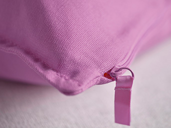Primer plano de un cojín rosa con cremallera y textura de tela gruesa.