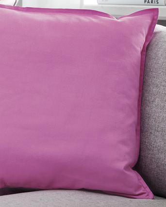 Cojín rosa liso con reborde decorativo sobre un sofá gris claro.