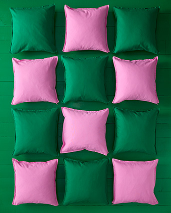 Doce cojines cuadrados, rosas y verdes, están ordenados simétricamente en una cuadrícula de tres por cuatro sobre tablas verdes.