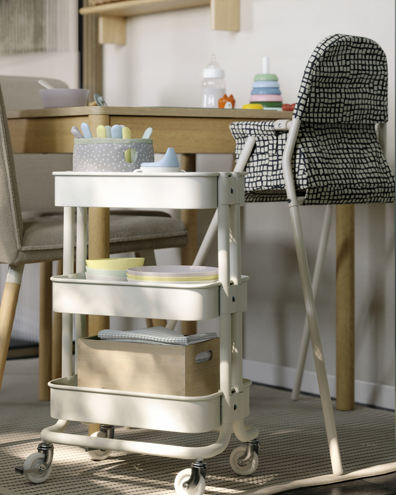 A white RÅSKOG trolley is placed next to a TONSTAD extendable table. It has baby-related items stored on the mesh shelves.