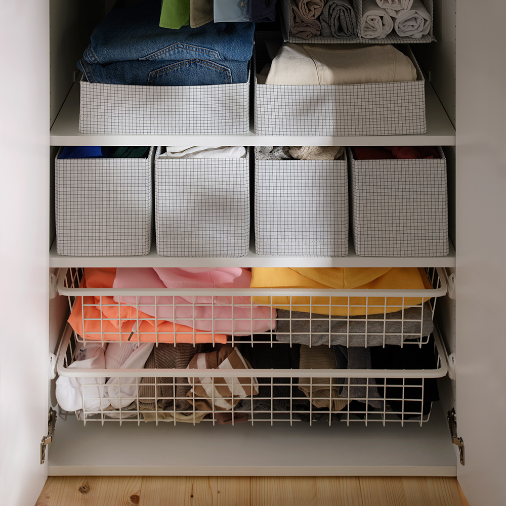 Un armario abierto con ropa doblada organizada dentro de cajas STUK con compartimentos, colocadas en los estantes y en cajones de alambre.