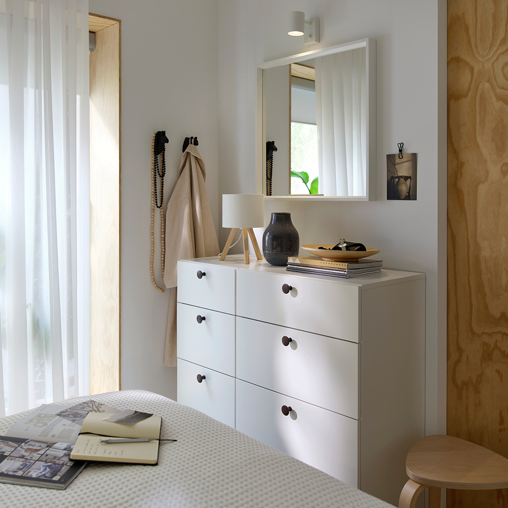 Un dormitorio con una cómoda LASTARE colocada debajo de un espejo de pared y decorada con varios objetos.