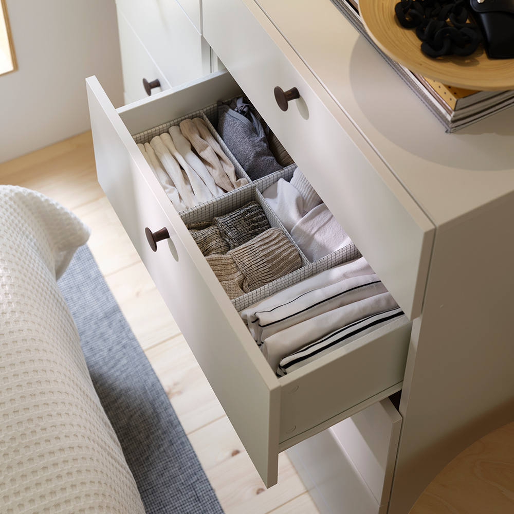 Un cajón abierto que muestra una caja STUK con compartimentos que organiza ropa doblada dentro de una cómoda blanca.