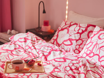 A bed with a white and bright pink floral HÄRLIR duvet cover and pillowcase and a bright pink GULLSTRÅLE bedspread.