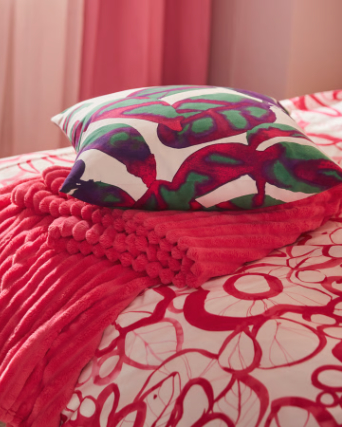 A close-up of a multicolour PELARKÖRSBÄR cushion cover placed on top of a bright pink GULLSTRÅLE bedspread.