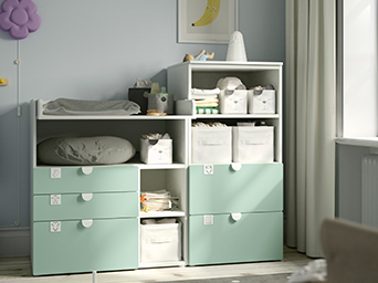 A changing table with a bookshelf in white and light green, filled with baby care items