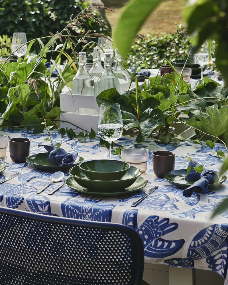 Un comedor en el jardín con un plato hondo PELARKAKTUS verde sobre una mesa decorada con follaje y vajilla.