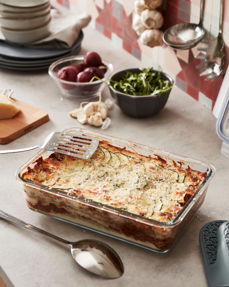 Escena acogedora de cocina con recipiente con tapa IKEA 365+ y utensilios de cocina GRUNKA junto a un platillo al horno.