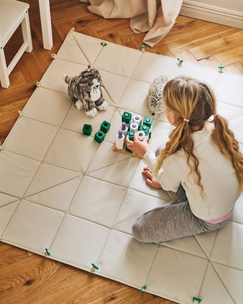 A child plays with a GREJSIMOJS board game on a GREJSIMOJS mat/storage box folded out to use as a mat.