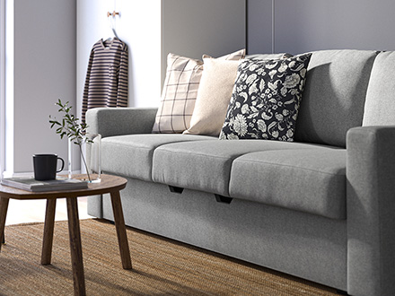 Sofá gris de tres plazas con cojines junto a una mesa de madera.
