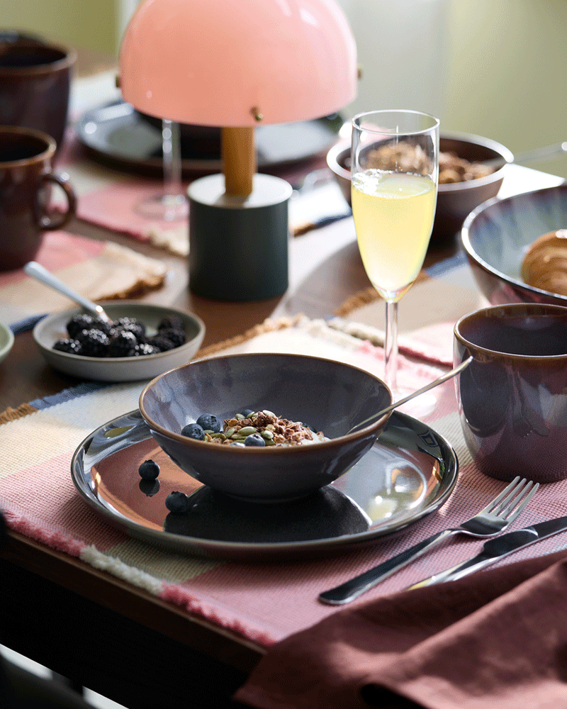 A bowl with yoghurt, muesli and blueberries are placed next to a lilac-coloured GLADELIG mug and a champagne flute.