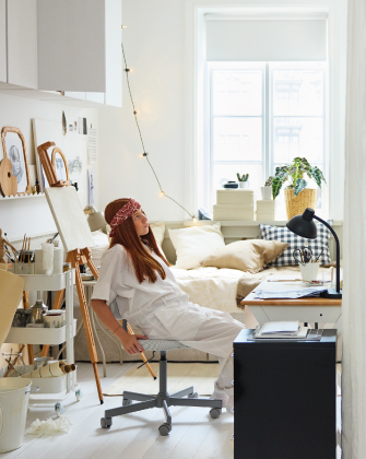 Person sitting in chair beside a neatly organized bedroom
