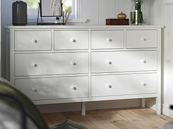 White dresser with open drawers, a pleated lamp on top, and a rustic wooden door in the background.