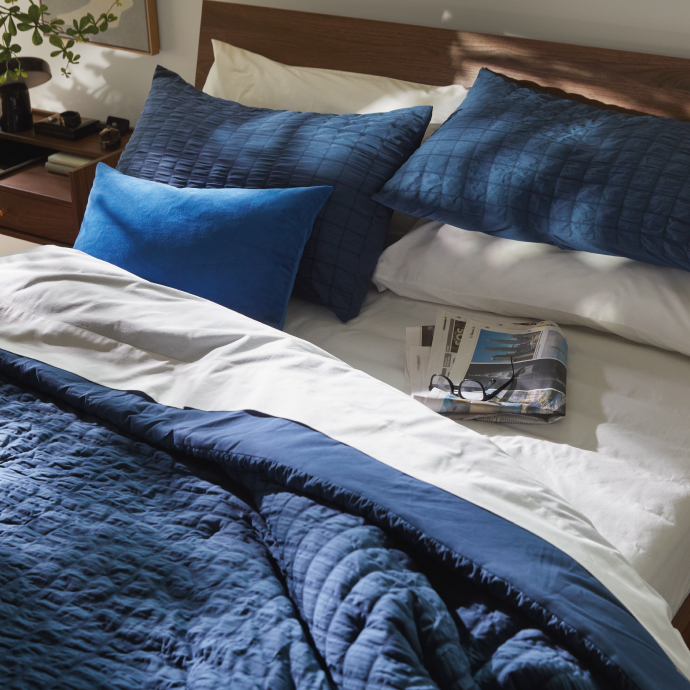 Neatly made bed with blue bedding and a magazine.