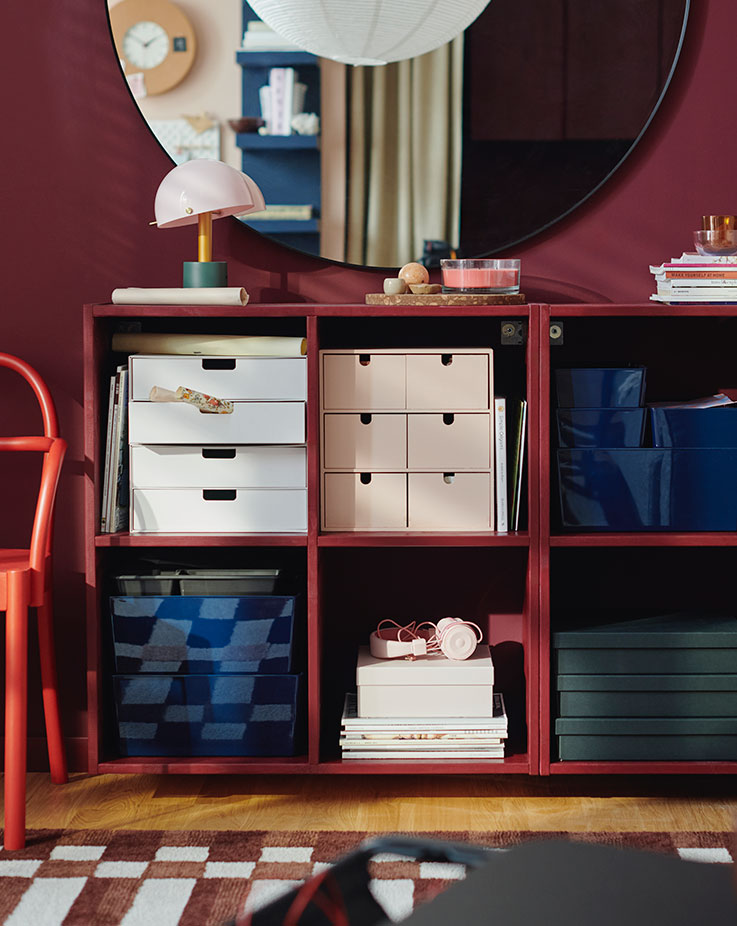 Two IVAR shelving units, painted red, containing a MOPPE mini chest of drawers and FJÄDERHARV storage boxes.
