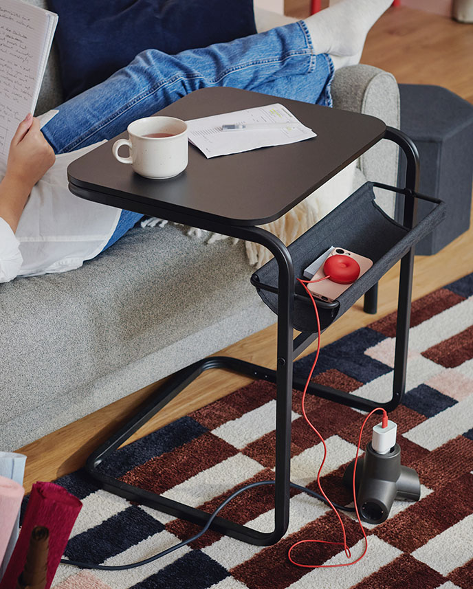 An OLSERÖD side table with a cup of coffee on top of it stands in front of a grey-beige sofa on top of a MARKBLÅMME rug.
