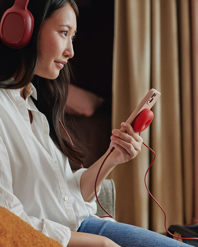 A person listens to music with headphones while charging a mobile phone with a VÄSTMÄRKE wireless charger.
