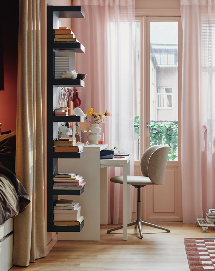 A dark beige KRYLBO swivel chair stands at a white LÄNGDHOPP pull-out desk near a window in a small living area.