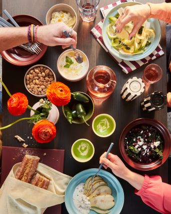 A top shot of a dining table with people eating from the SPJUTLILJA bowls and plates and drinking from the yellow cups.