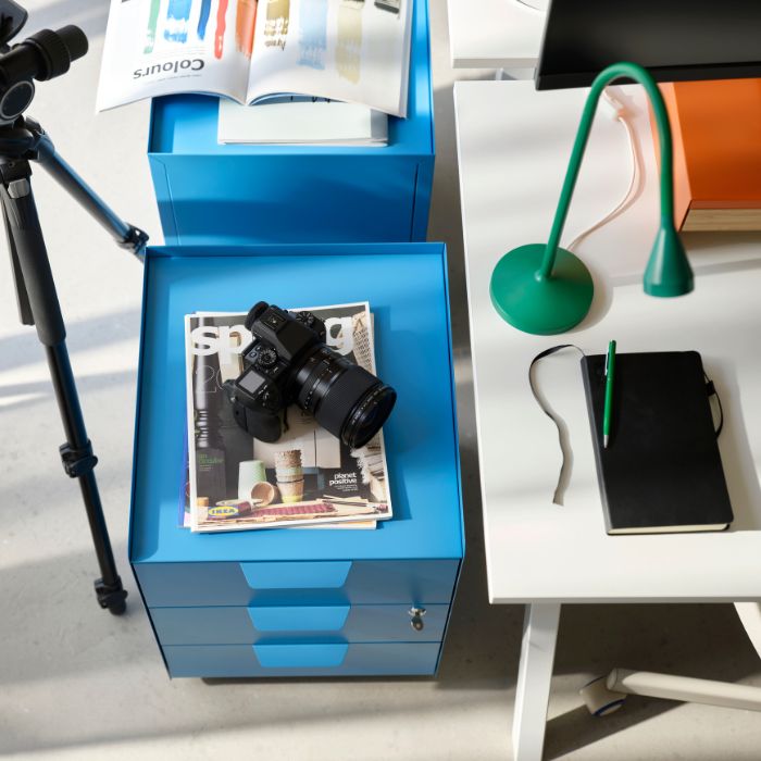 Espacio de trabajo moderno con escritorios TROTTEN, lámpara NÄVLINGE, cajones de almacenaje y cámara en oficina funcional.