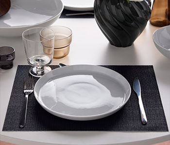 A place setting with an IKEA 365+ plate, an IKEA 365+ goblet and PRAKTBOTIA cutlery and a light brown OLIVTRAST glass.