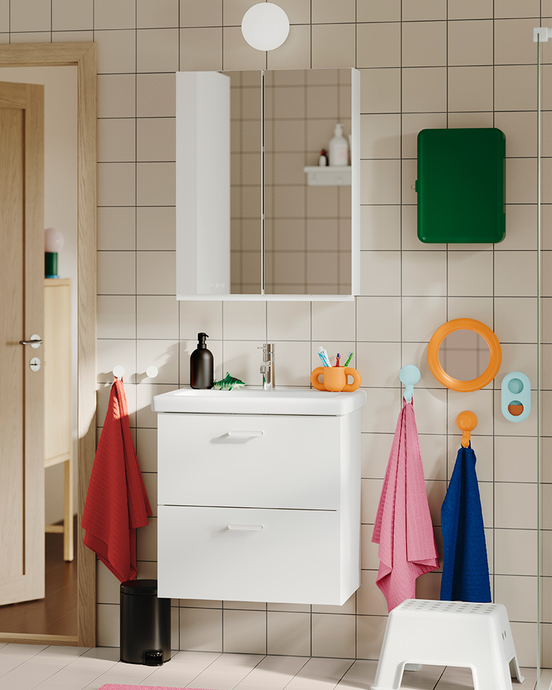 A tiled bathroom featuring the white TVÄLLEN/ENHET washstand with two drawers, wall-mounted with colourful towels nearby.