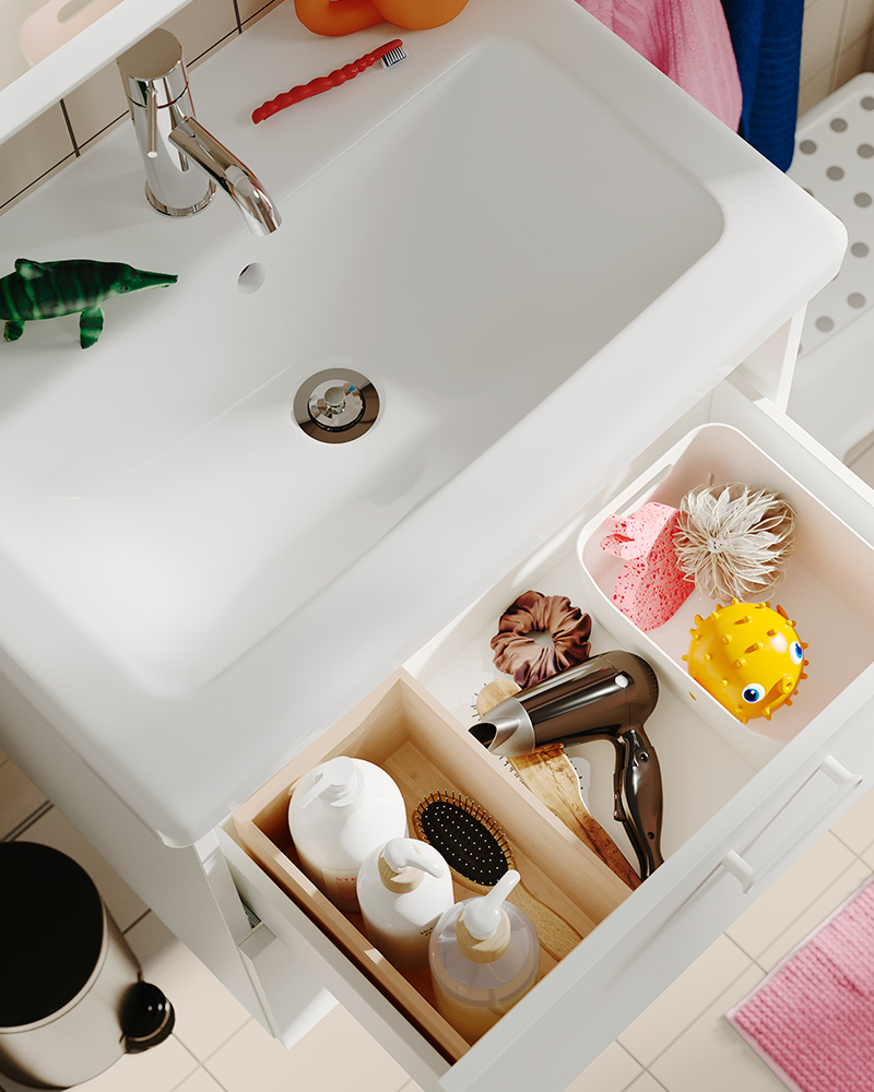 An UPPDATERA storage box, placed inside an open drawer in a bathroom, holding a hair dryer, brush and toiletries.
