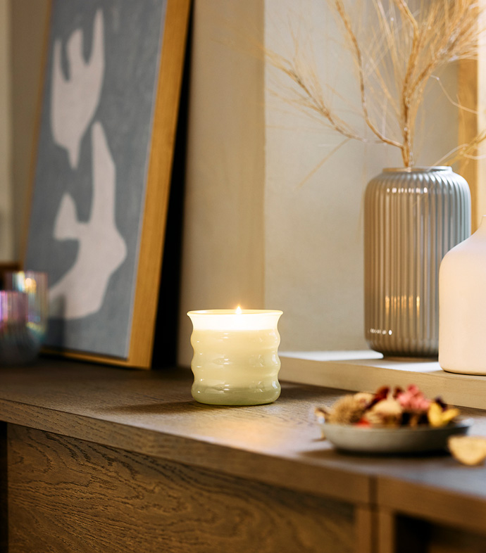 Una vela encendida sobre un mueble de madera, rodeada de decoración elegante, creando un ambiente cálido y acogedor.