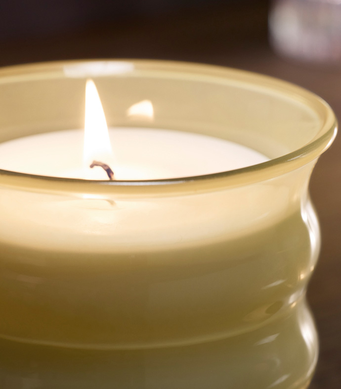 Una vela encendida sobre un mueble de madera, rodeada de decoración elegante, creando un ambiente cálido y acogedor.