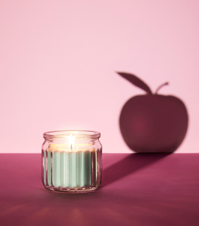 Vela encendida proyectando una sombra de manzana sobre un fondo rosa. Creativa, minimalista, estética y con una iluminación suave.