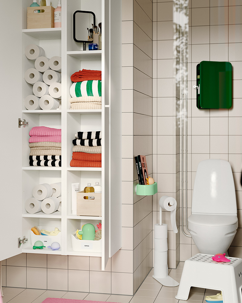 A tiled bathroom with the white ENHET high cabinet with doors, shelves filled with towels, toilet rolls and storage boxes.
