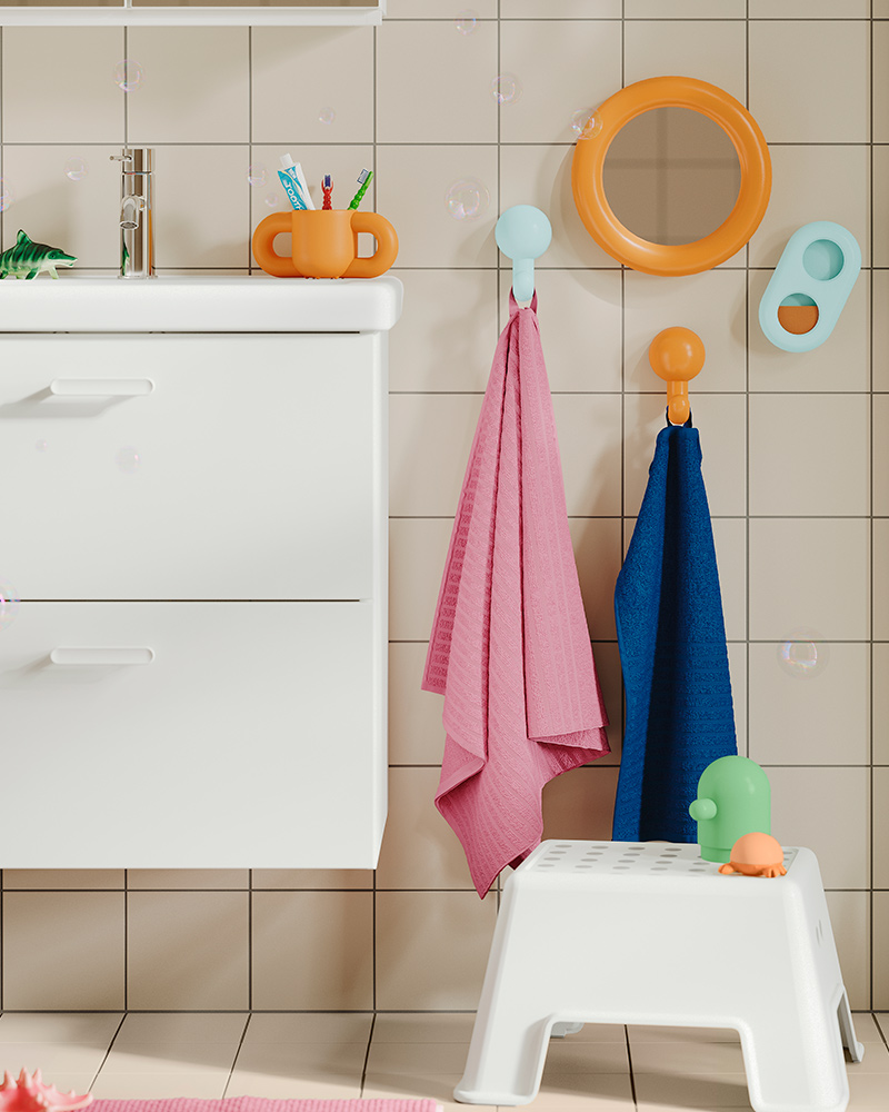 A BOLMEN step stool on the floor, a sink and colourful towels and accessories on the wall in child-friendly height.