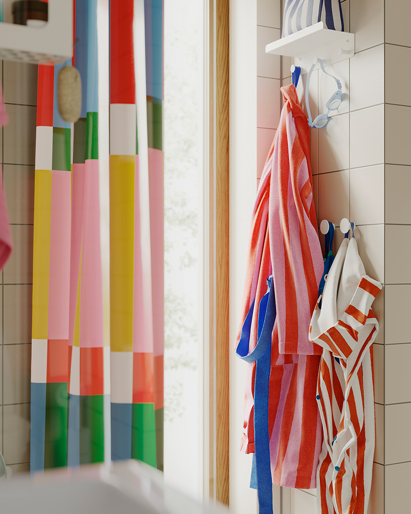 A bathroom with an ENUDDEN wall shelf with 3 hooks, holding striped towels and colourful robes on a tiled wall.