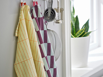 Paños de cocina y utensilios colgados en un estante magnético. Ventana luminosa con una planta al fondo.