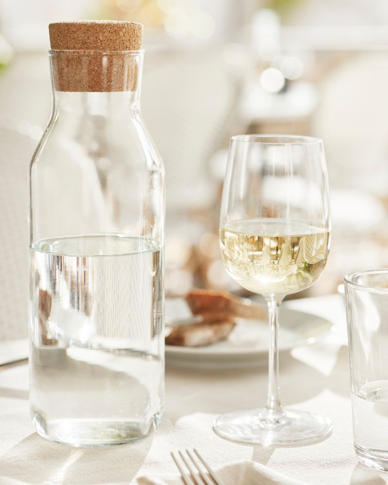 Bright restaurant table setting with STORSINT wine glass, IKEA 365+ glass and plate, DRAGON fork, and KORKEN bottle.