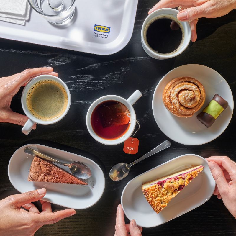 Pictured are coffee mugs, a teacup, a cinnamon roll, a chocolate cake, an apple-blueberry pie, and a white tray with the IKEA logo.