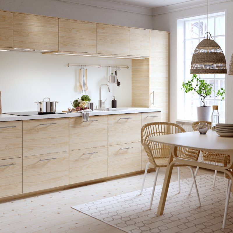 Cocina moderna y espaciosa con puerta a un jardín, los frentes de los cajones son de bambú, tiene colores blancos, se ven los hornos y la encimera de la cocina.