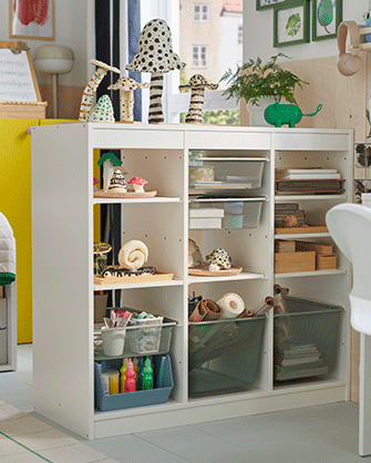 A white multi-compartment storage shelf unit filled with craft supplies, books, and translucent green plastic bins.