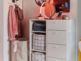 A white chest of drawers and shelving unit with fabric storage boxes, lit by an arched neon lamp next to a laundry basket.