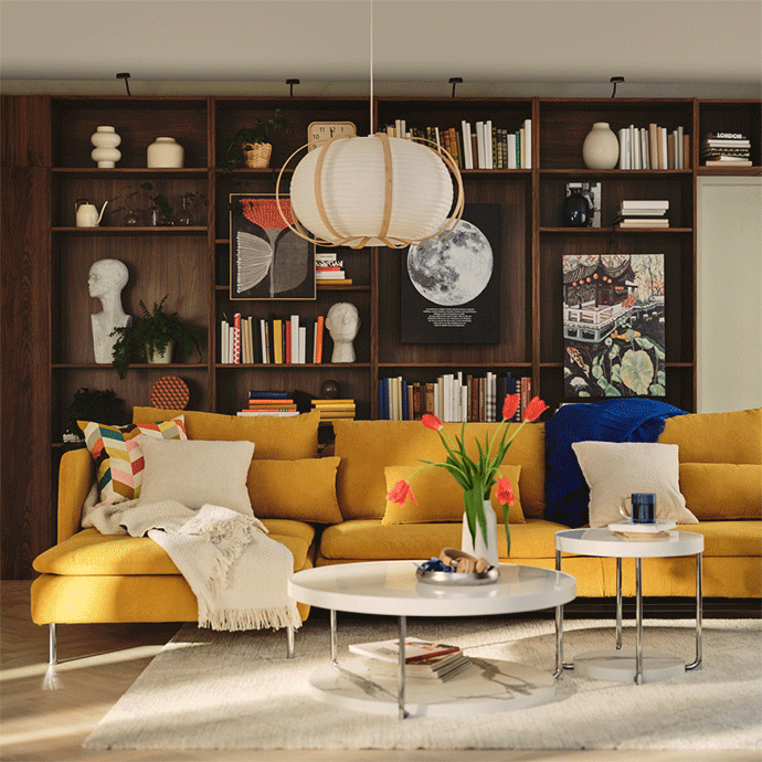 Salón acogedor con un gran sofá modular amarillo, dos mesas de centro blancas con tulipanes rojos y una librería de pared completa en madera oscura.