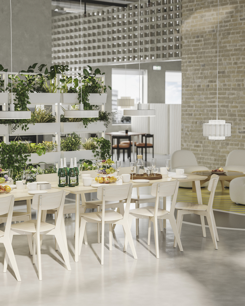 A sunny office dining area with white tables and wooden chairs, flanked by plant stands with cascading greenery