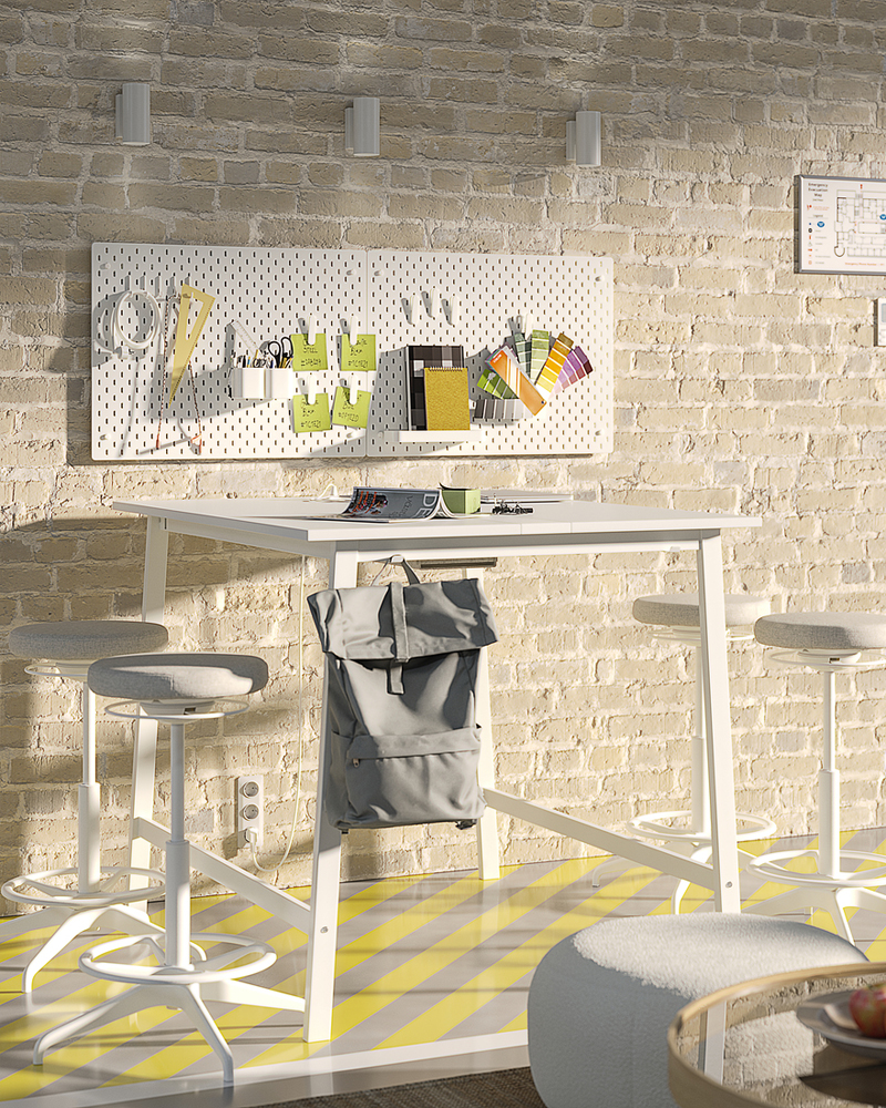 White standing table with four high stools, set against a lightbrick wall with pegboard containing art materials.