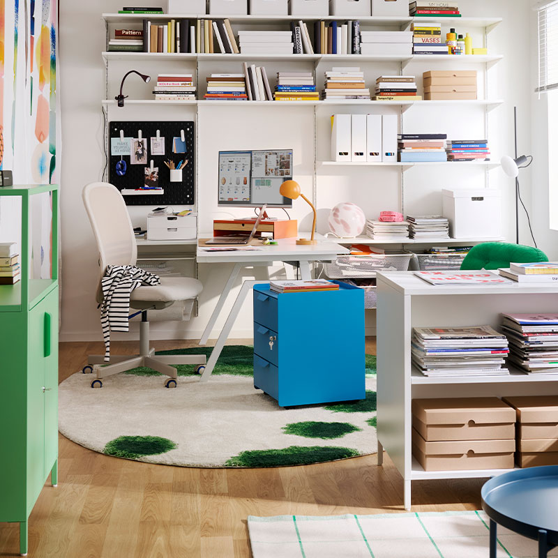 A home office features a blue TROTTEN drawer unit on castors, surrounded by shelves and a desk with stationery.
